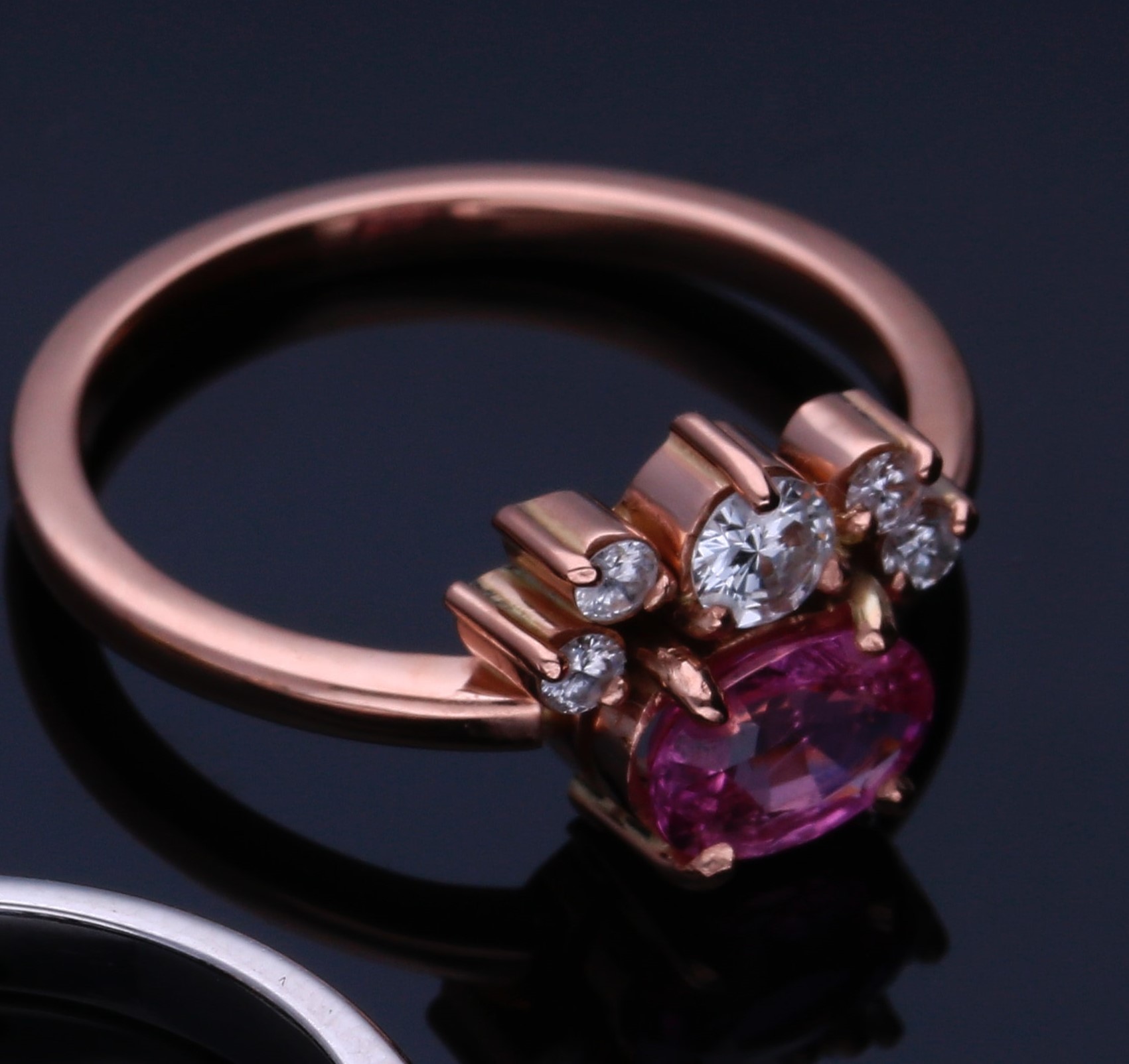 Fotografía de un anillo de color rosa metalico con diamantes blancos y rosas en un fondo oscuros 