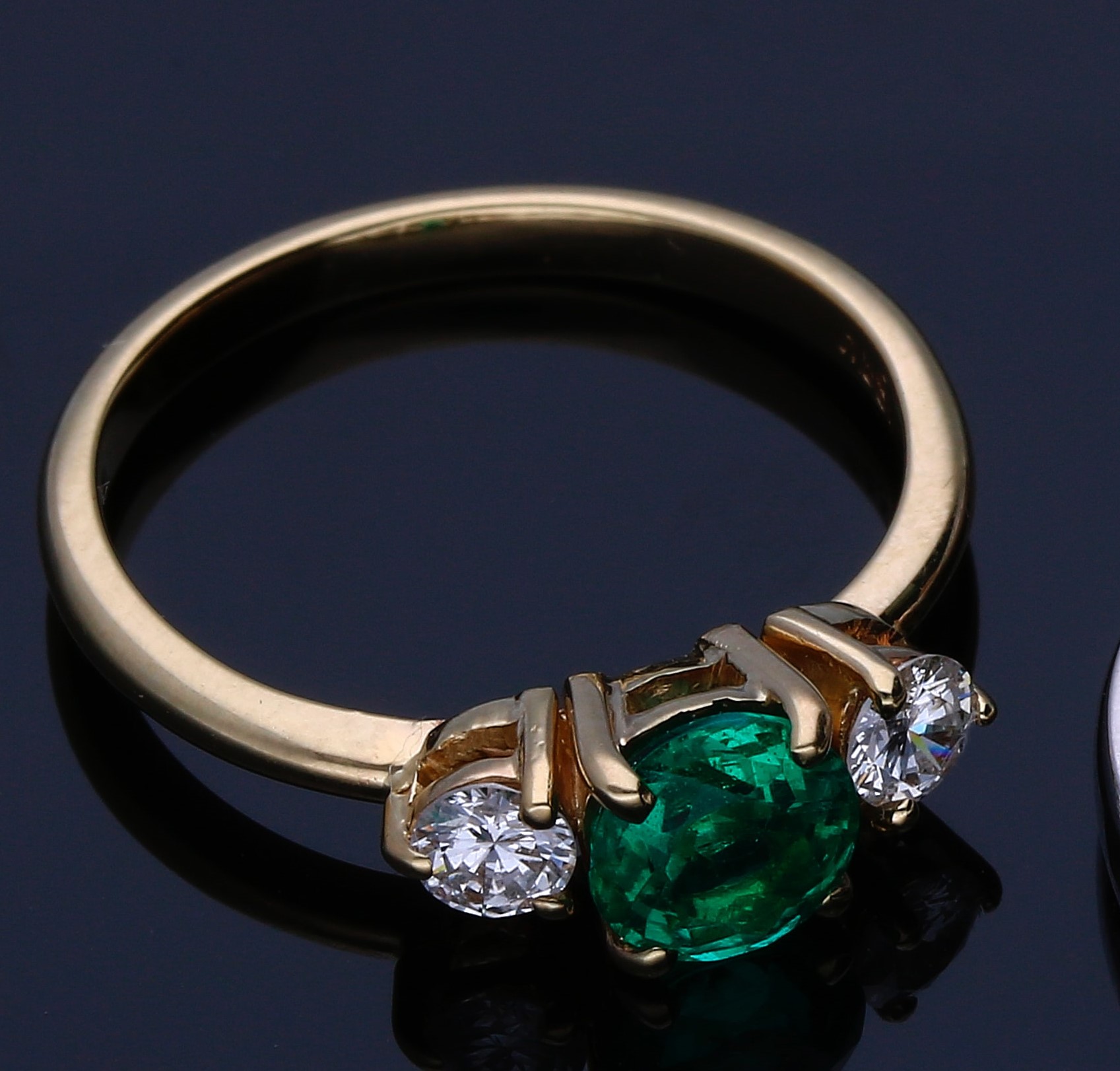 Fotografía de un anillo dorado con diamantes blancos y uno color  verde en el centro en un fondo oscuro