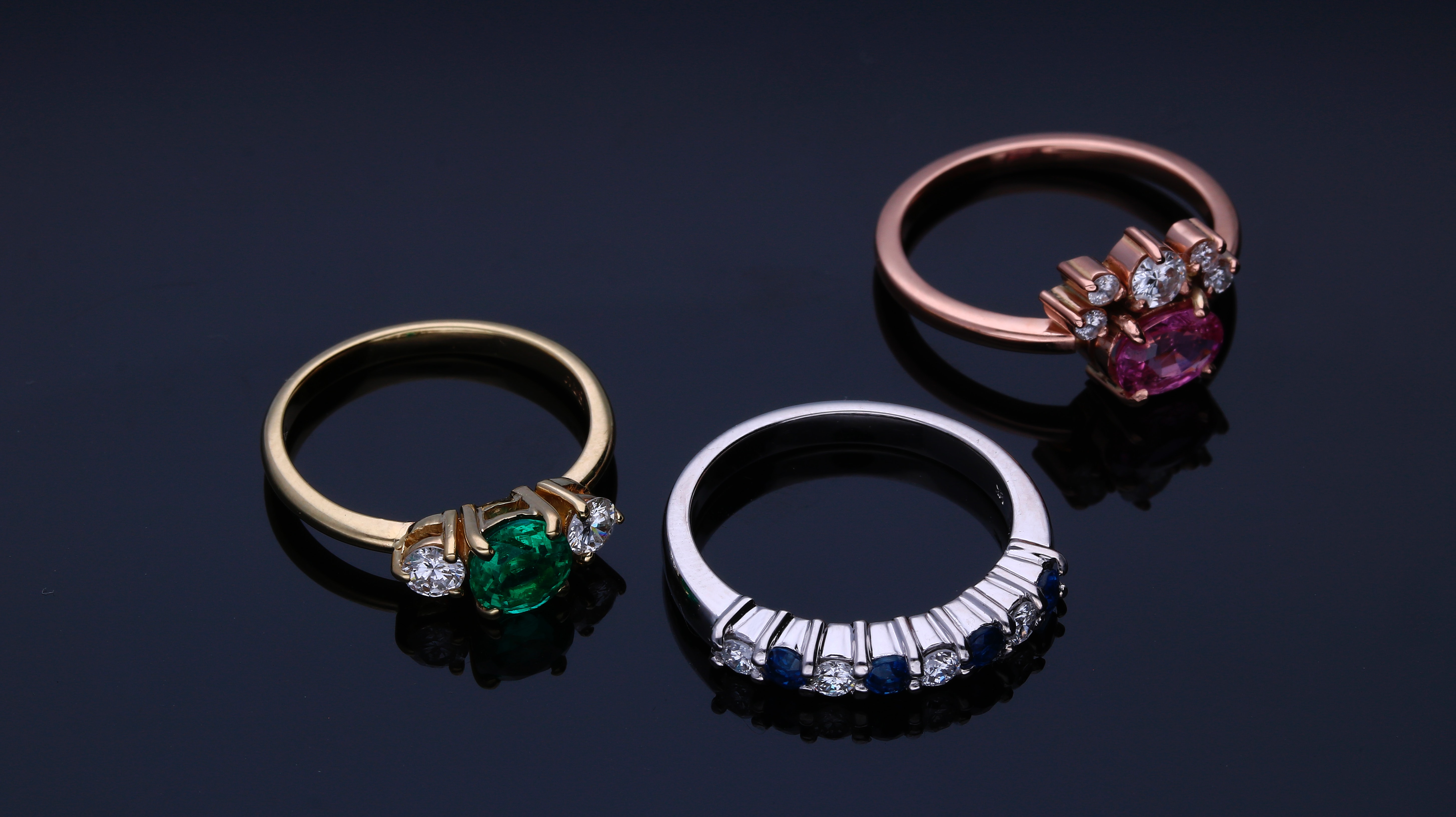 Tres anillos con diamantes, uno de plata y los otros en metal rosado, sobre una seuperficie en un fondo con tonos claros