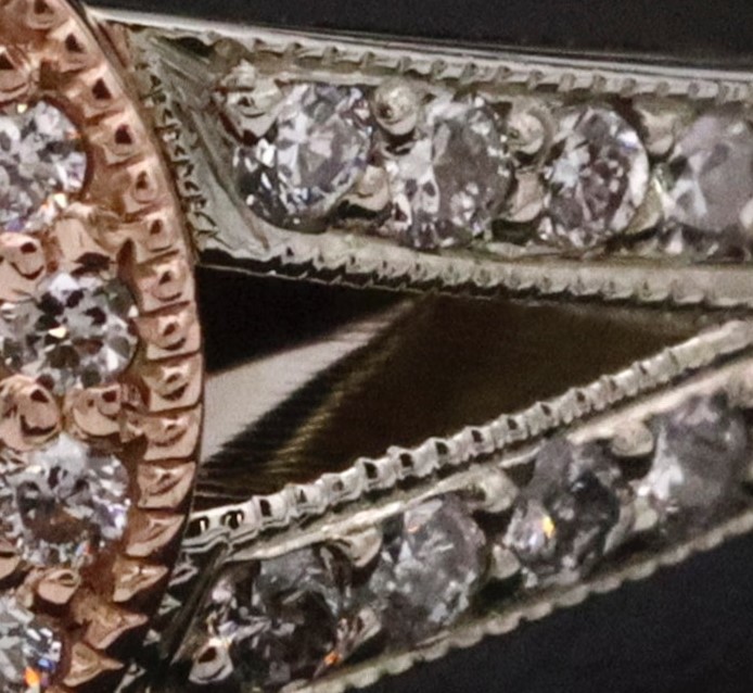 Fotografía de un anillo de color rosa metalico con diamantes blancos y rosas en un fondo oscuros 