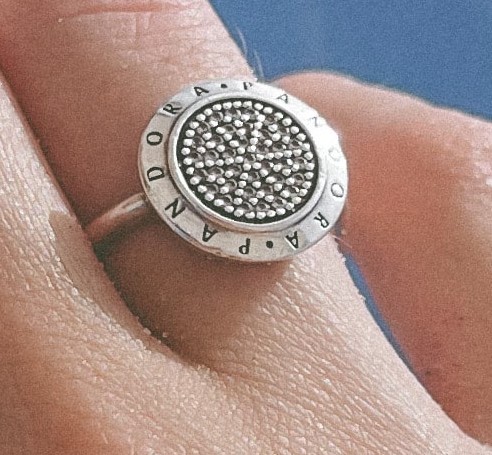 Fotografía de un dedo con acercamiento al anillo de plata con forma redonda y letras en su alrededor