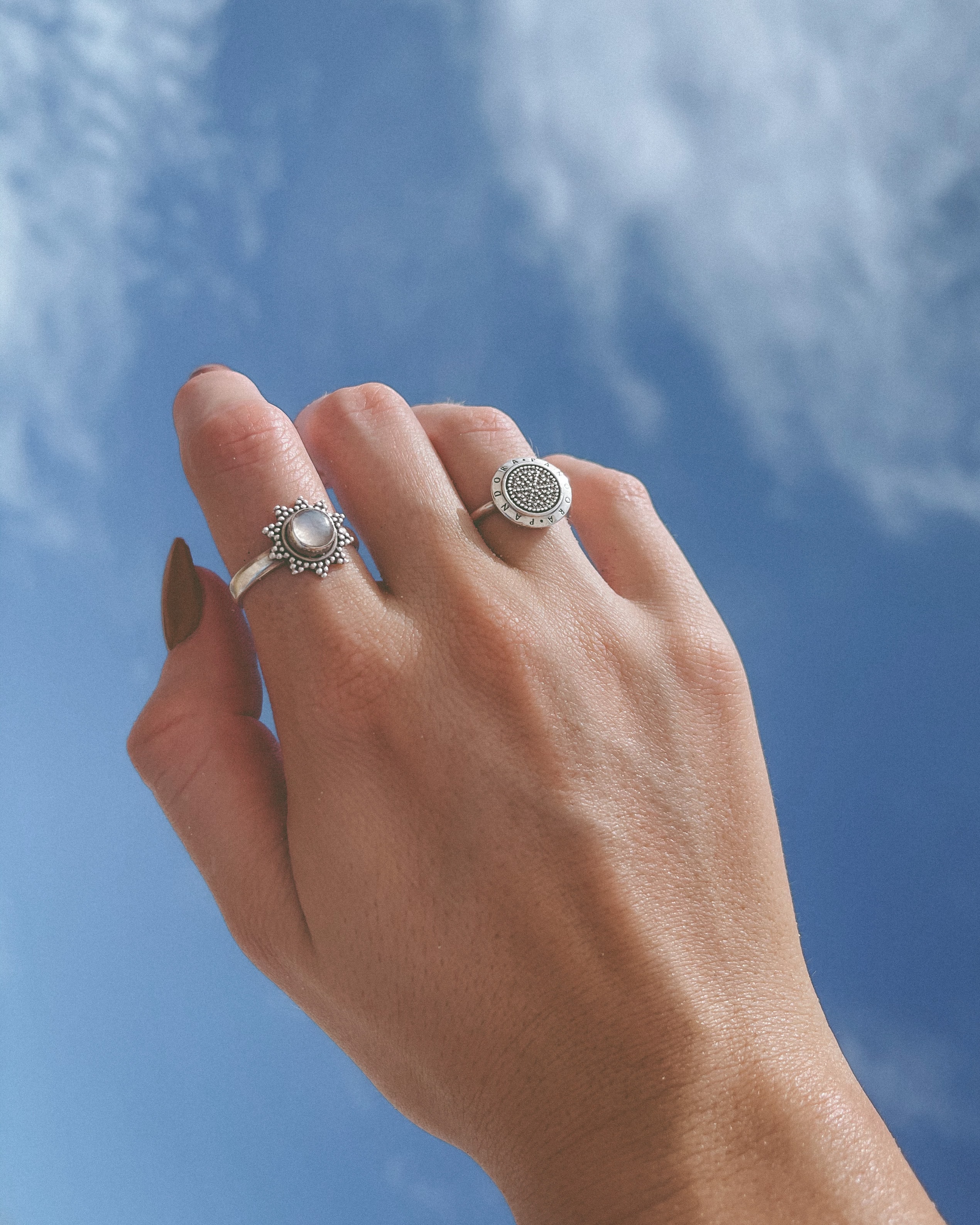 Fotografía de una mano en el aire con dos anillos de plata y de fondo un cielo azul