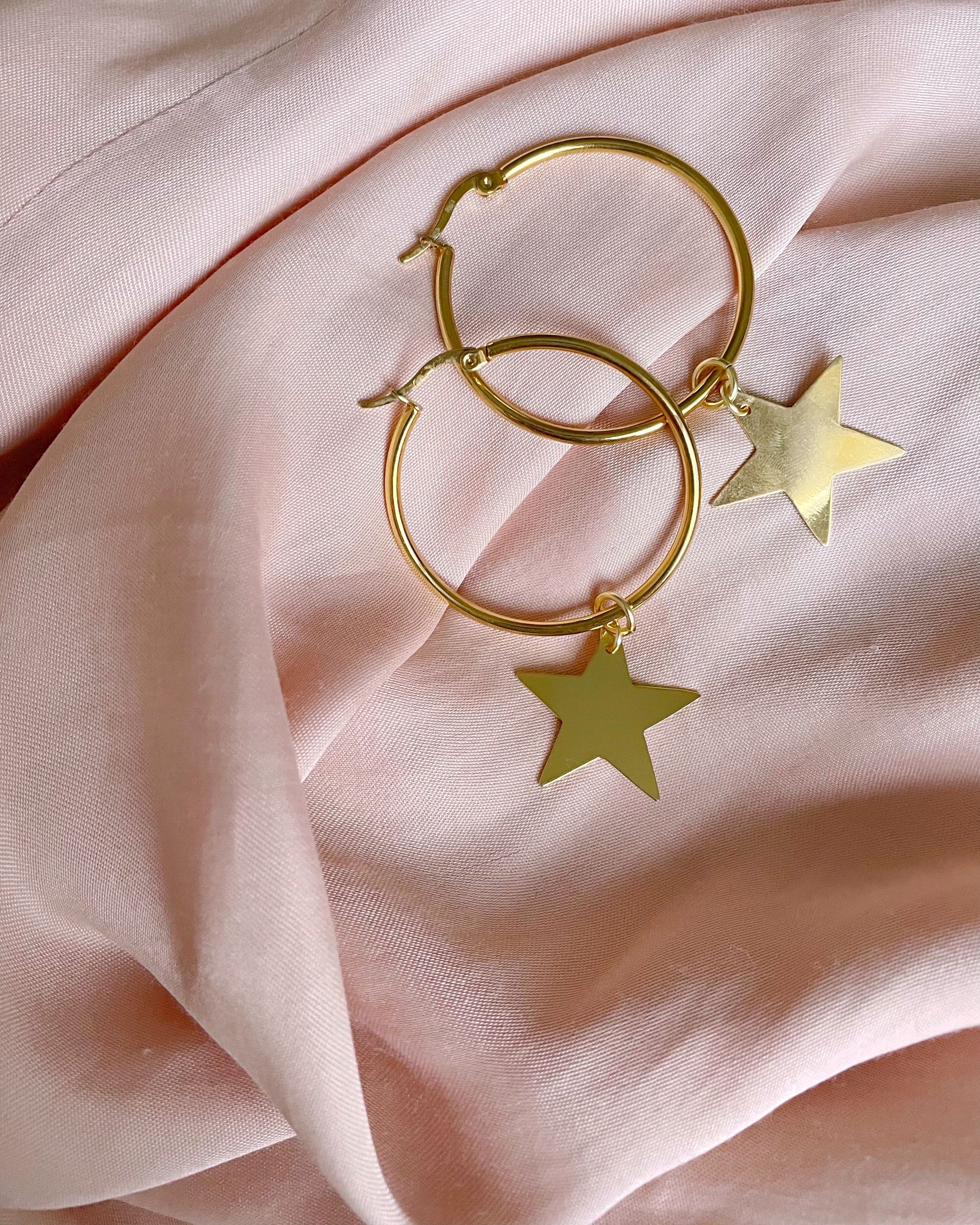 Par de aretes de estrellas doradas sobre una tela rosa