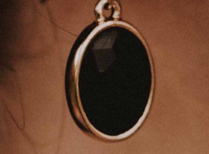 Fotografía de una pieza ovalada de color negro y alrededor de metal que esta colgando 
