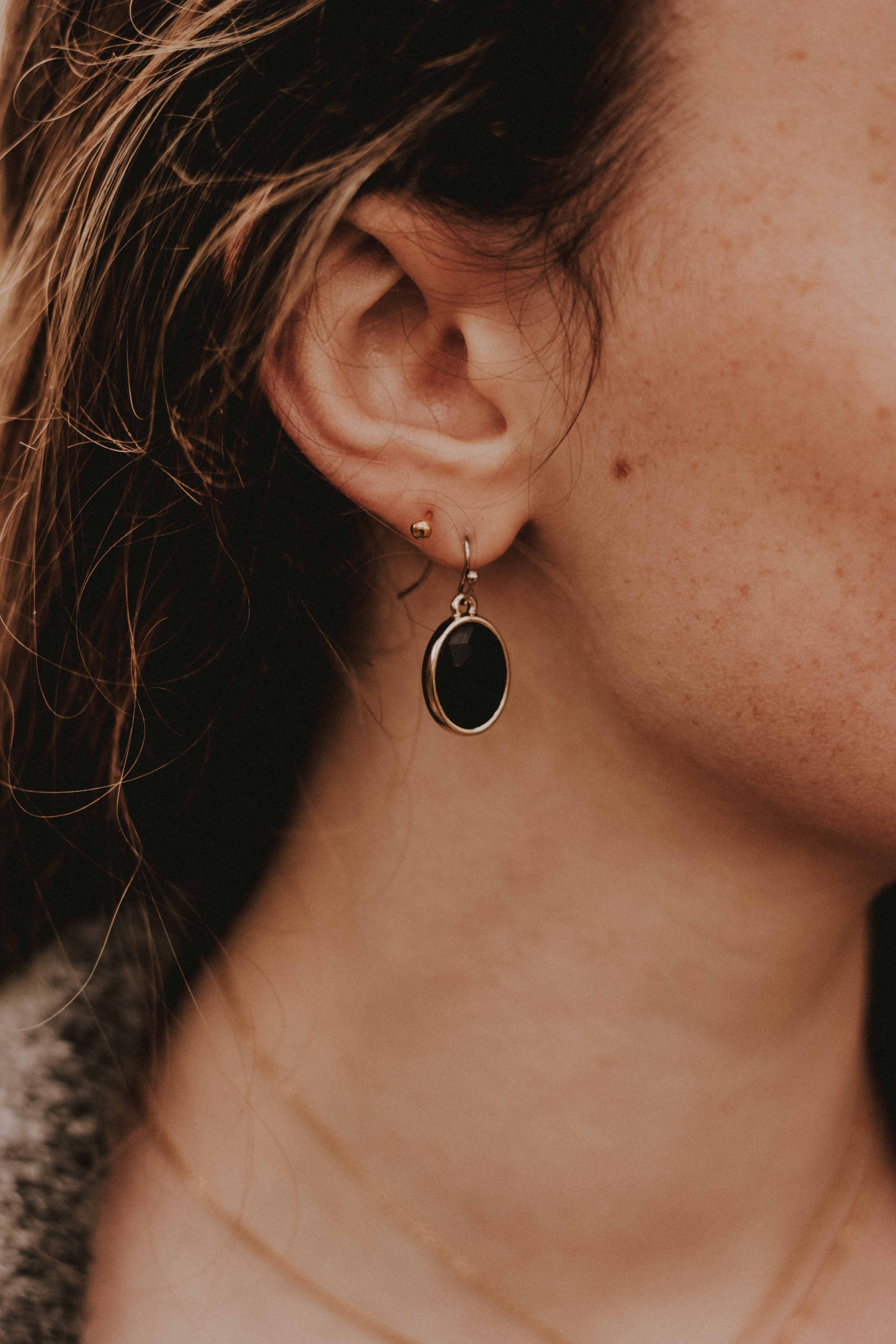 Fotografia de la oreja de una mujer con un arete colgando de forma redonda de color negro 