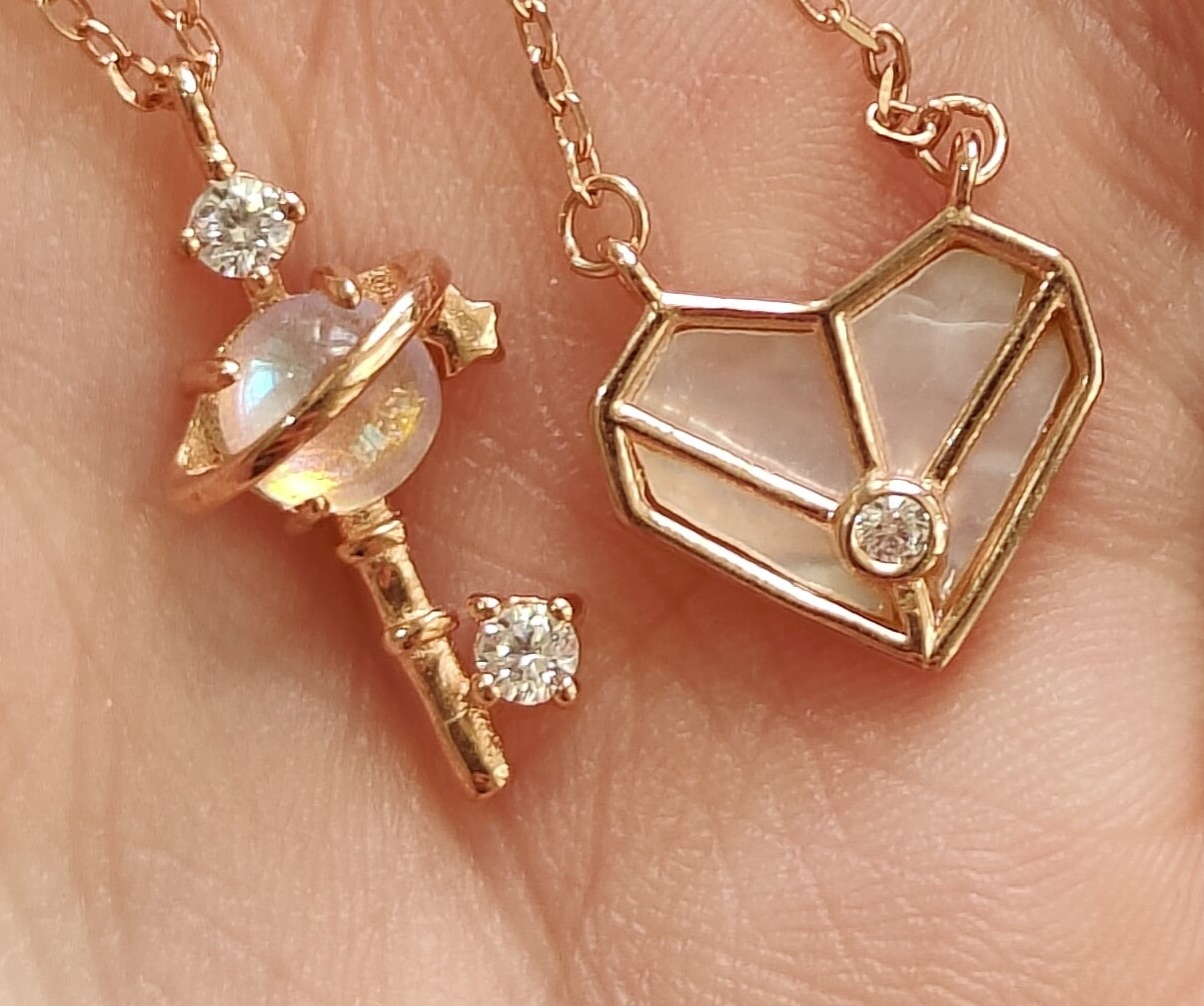 Fotografía de dos dijes de un collar uno en forma de corazon y otro en forma de paleta color dorados con diamantes cristalinos