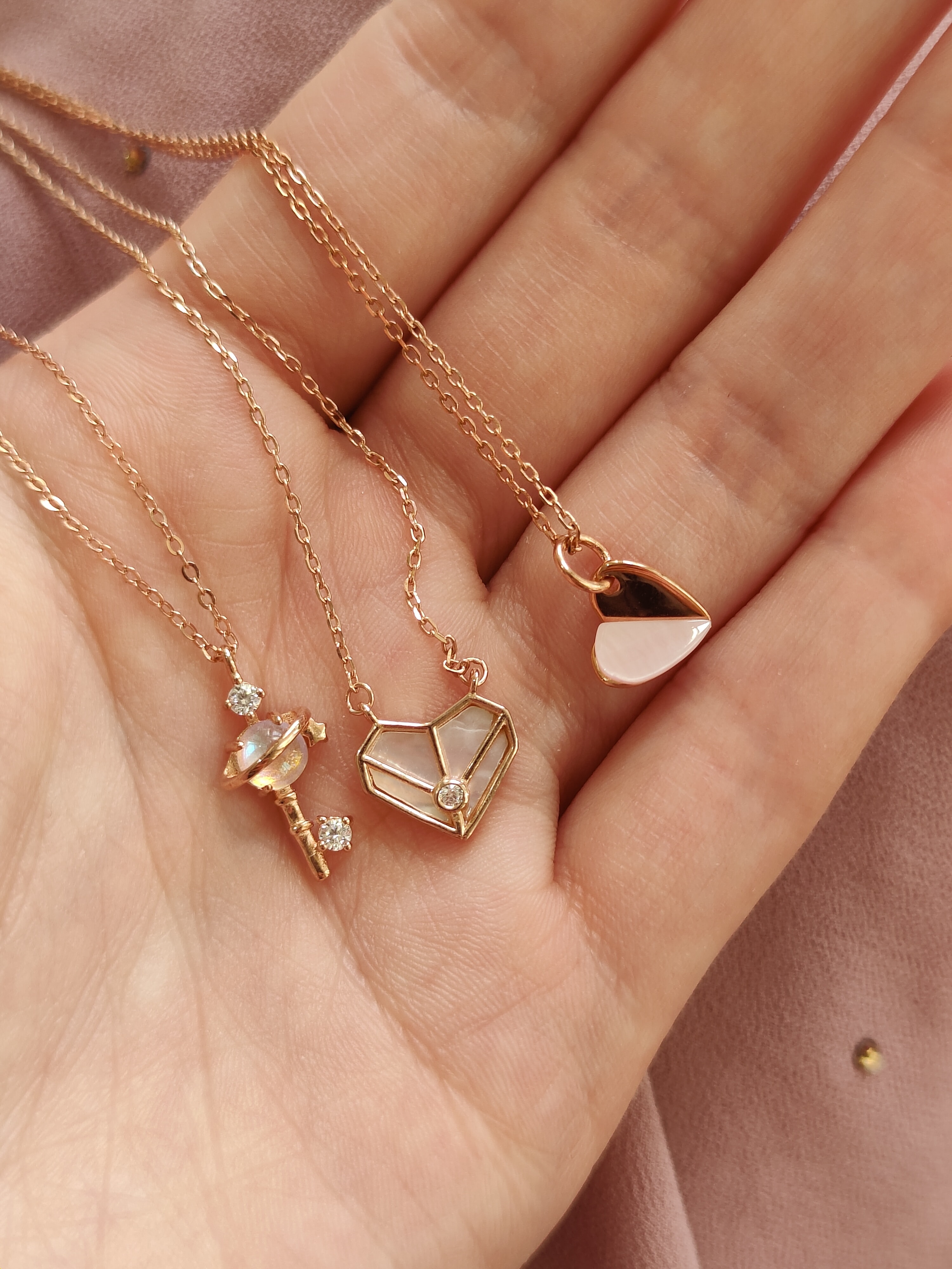 Tres collares dorados sobre una mano, los cuales tienen forma de corazon y paleta con diamantitos incrustados 